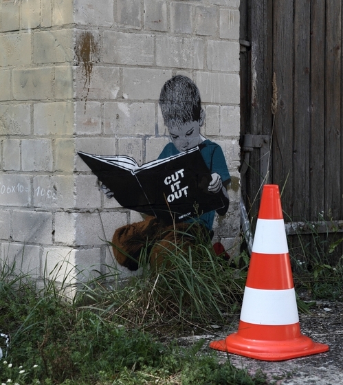 Wandmalerei: kleiner Junge liest Banksys Buch "Cut it out"
