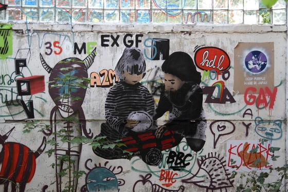 vielseitig gestaltete Wand, in der Mitte ein Poster zweier Kinder, die mit einer Bombe spielen
