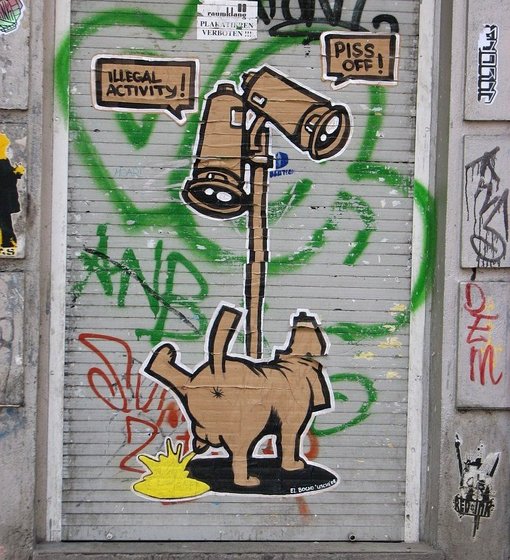 Hund pinkelt an einen Mast mit Überwachungskameras, Schrift "Illegal Activity" und "Piss off"