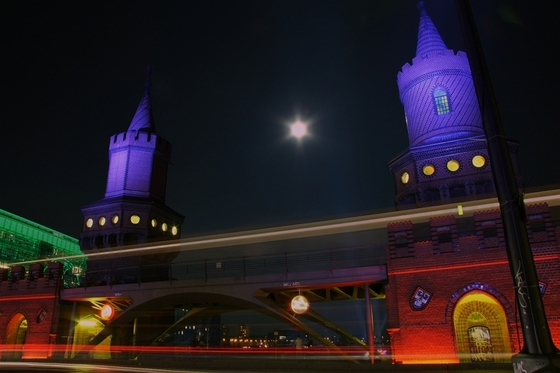 Langzeitbelichtung der bunt angestrahlten Oberbaumbrücke, Mond zwischen den Türmen