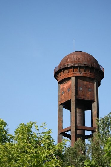 die Spitze eines Wasserturms ragt hinter ein paar Bäumen hervor