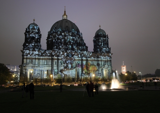 Berliner Dom, angestrahlt mit einem Motiv mit vielen Gesichtern