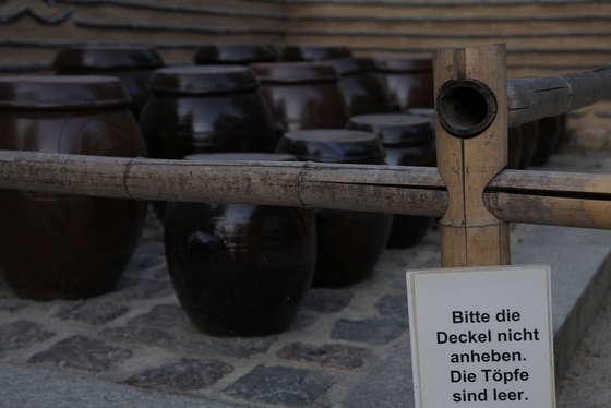 Keramik-Krüge hinter einer Absperrung, Schild "Bitte die Deckel nicht anheben. Die Töpfe sind leer."