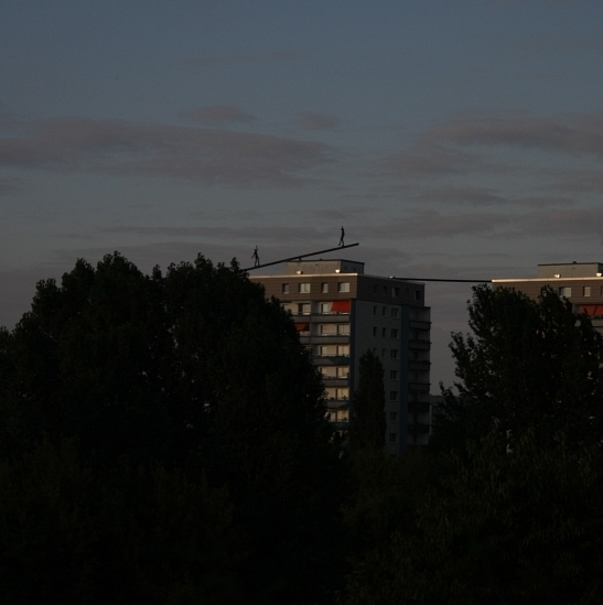 zwei Hochhäuser, auf deren Dach stilistisch Menschen auf Balken balancieren