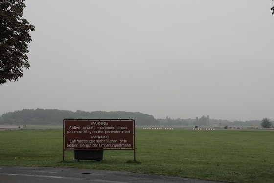 zweisprachiges Schild "WARNUNG, Luftfahrzeugbetriebsflächen, bitte bleiben sie auf der Umgehungsstrasse"