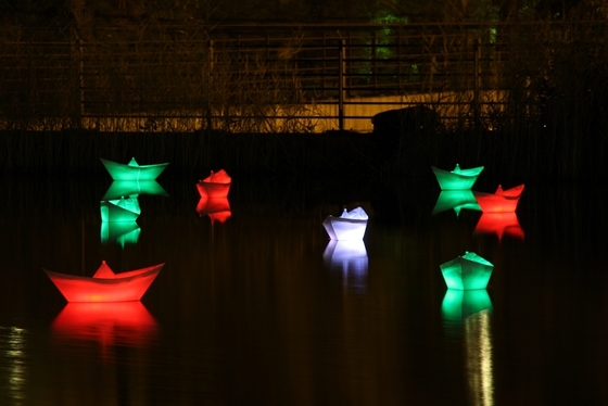 bunt beleuchtete Falt-Schiffchen auf einer Wasserfläche