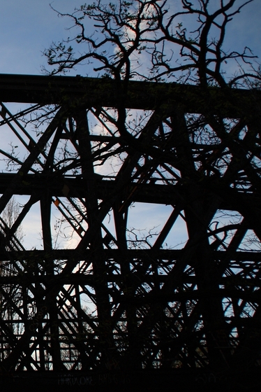 Silhouette einer Fachwerkbrücke und eines knorrigen Baums vor blauem Himmel