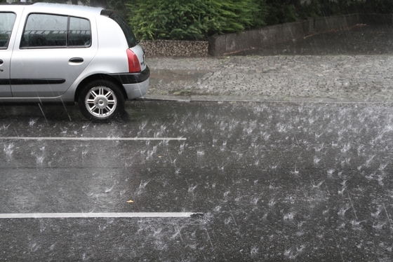 Straße mit geparktem Auto, ströhmender Regen