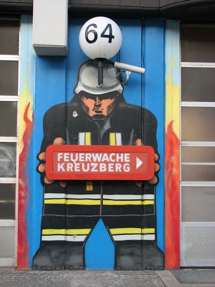Feuerwehrmann hält Schild mit Text "Feuerwache Kreuzberg"