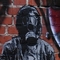 gestaltete Backsteinwand: Spraydose, daneben ein Mann in Gasmaske